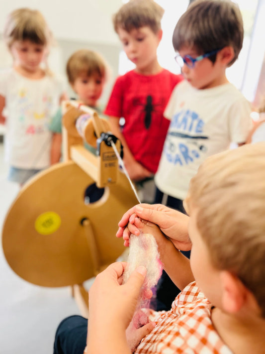 Crianças acompanham uma demonstração de fiação da lã numa roda de fiar.